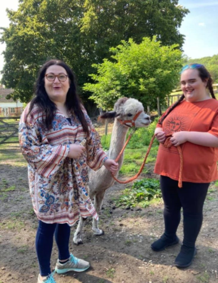 Two smiling young women walking an alpaca on a sunny day