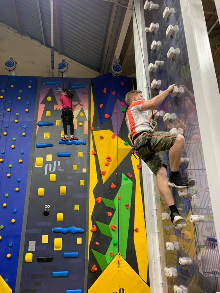 A teenager climbing an indoor climbing wall, with a younger child on another route