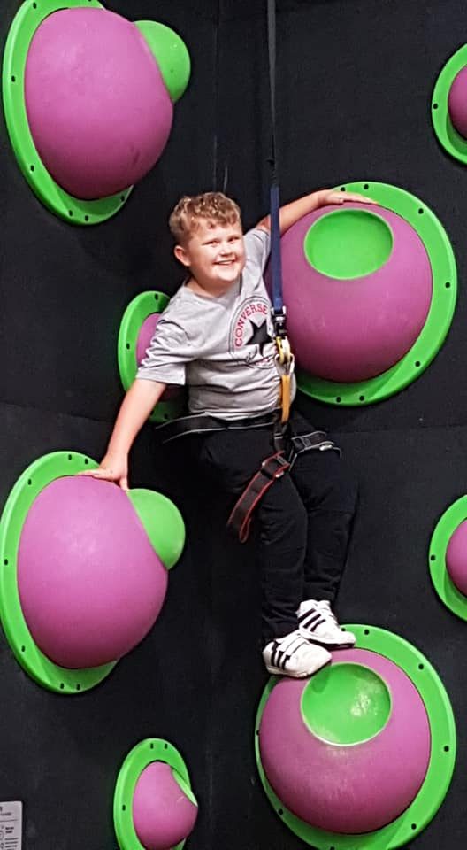 A smiling boy in a harness on a clip-and-climb wall