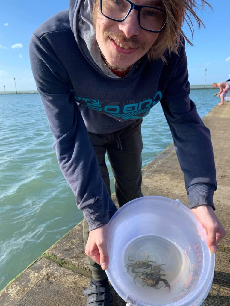 A smiling young man holding a bucket of crabs on a seafront harbour wall