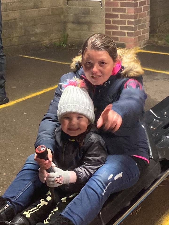 A mum and her toddler on a toboggan at night, both smiling