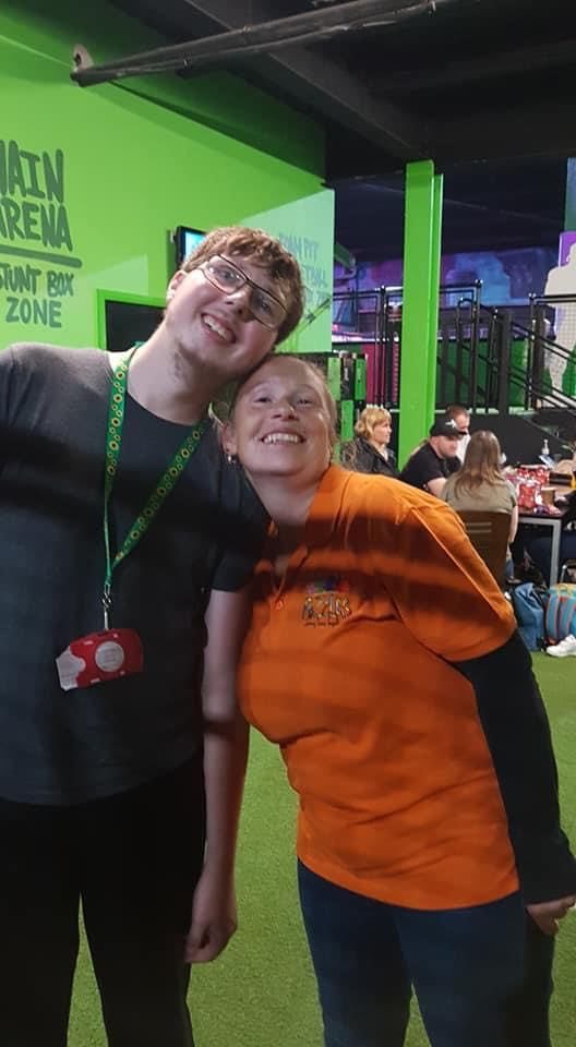 A smiling young man and a Puzzles staff member in an orange shirt at a trampoline park