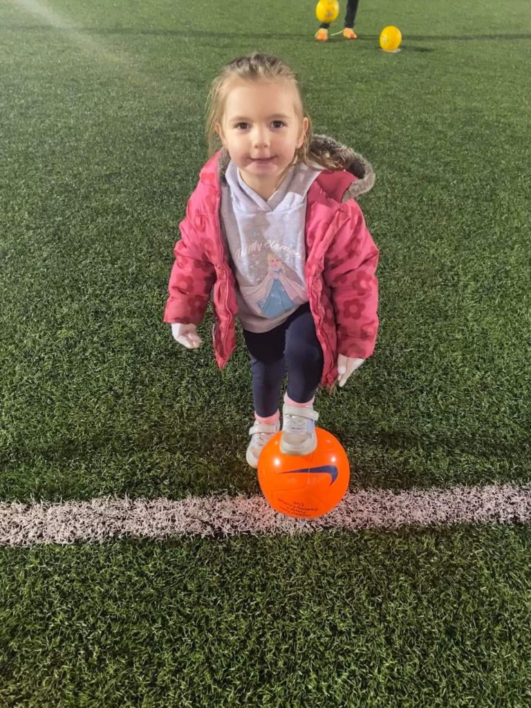 A young girl with her foot on an orange Puzzles football